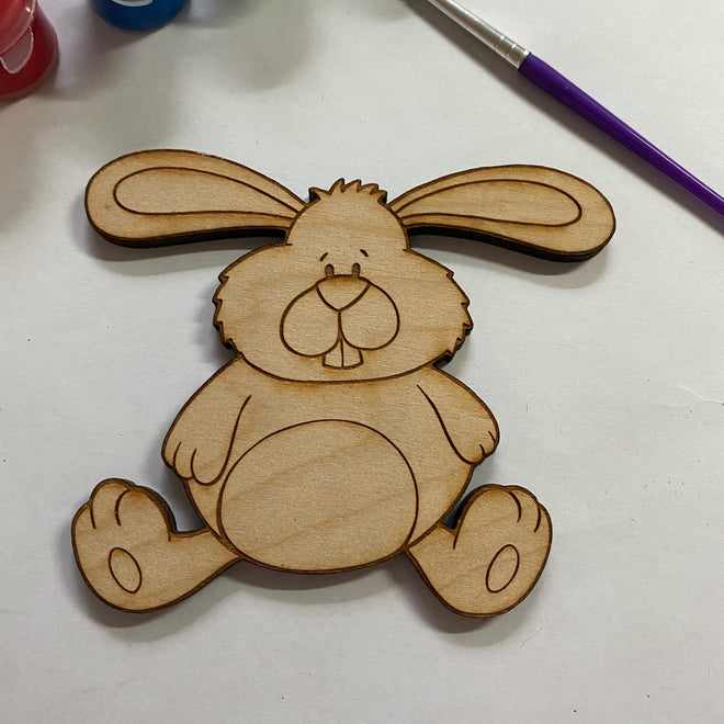 Wooden rabbit cutout with paint containers and a brush on a white surface
