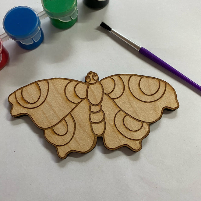 Wooden butterfly ornament with paint containers and a brush on a white surface