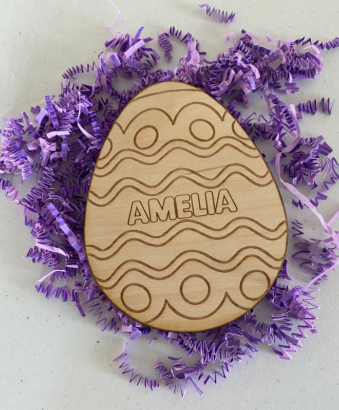 Wooden Easter egg ornament with 'AMELIA' engraving on a purple decorative background
