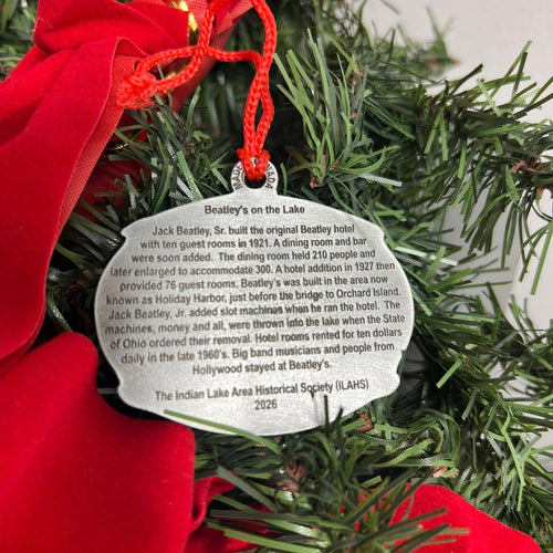 Decorative ornament with a red ribbon on a Christmas wreath, featuring text about the history of the Beatley's on the Lake.