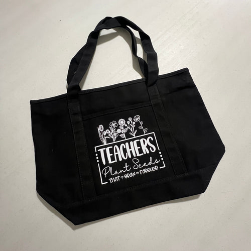Black tote bag with white text and graphics on a white background