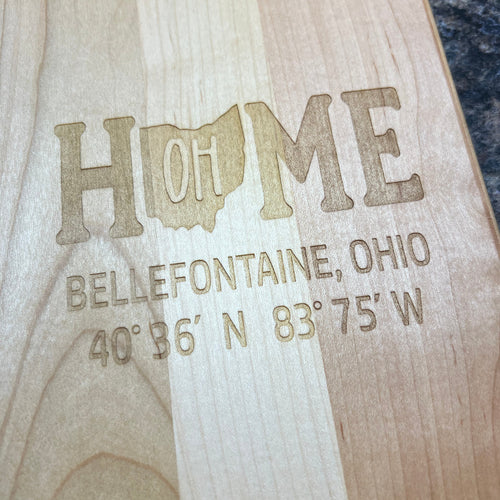 Wooden sign with engraved text 'HOME' and coordinates on a dark surface