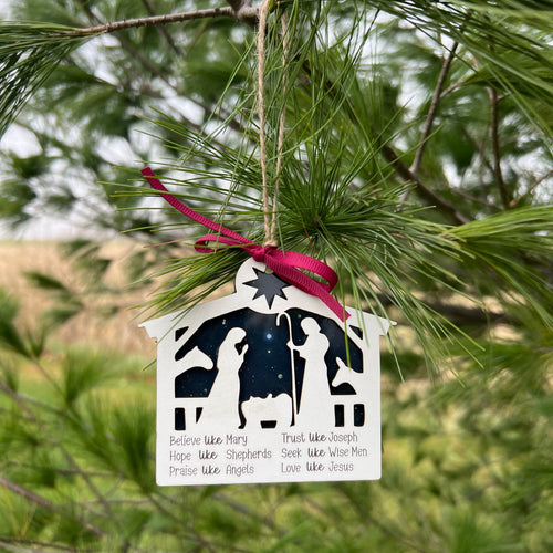Decorative ornament with silhouettes of people and animals hanging from a pine tree.