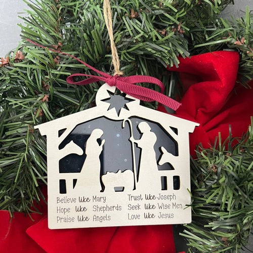 Decorative nativity scene ornament with religious text on a green wreath.