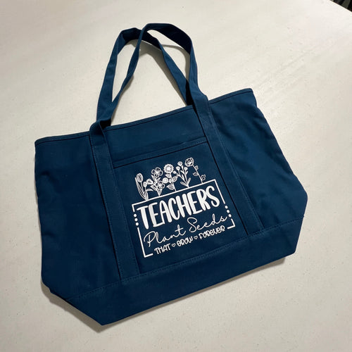 Navy blue tote bag with 'Teachers Plant Seeds' text on a white surface
