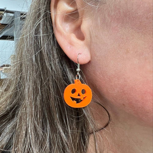 Close-up of an orange pumpkin-shaped earring worn by a person with long hair.