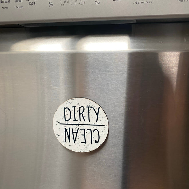 A round white magnetic sticker with the words 'DIRTY CLEAN' in black lettering, shown on the stainless steel door of a dishwasher.
