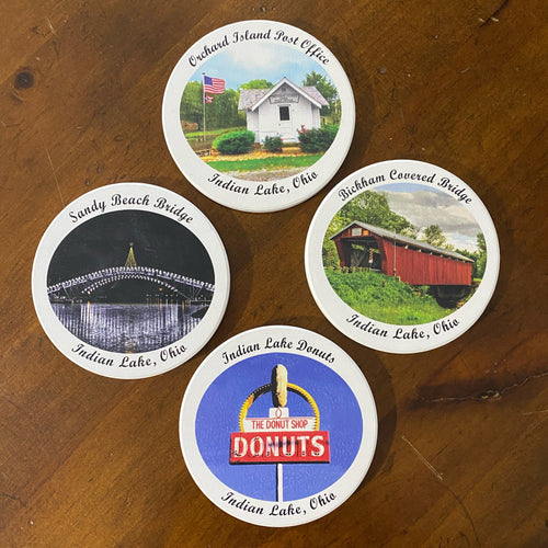 Four coasters with scenic and branded images on a wooden surface
