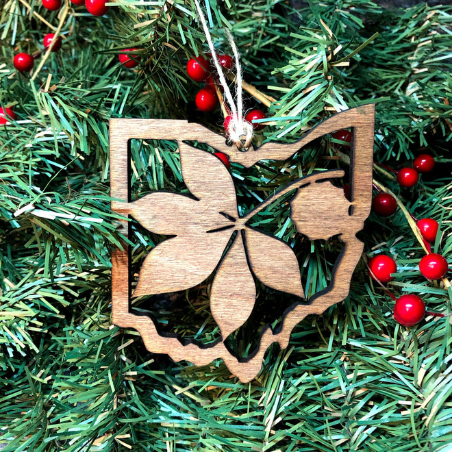 A wooden cutout Christmas ornament shaped like the state of Ohio, hanging on a green artificial Christmas tree with red berries.